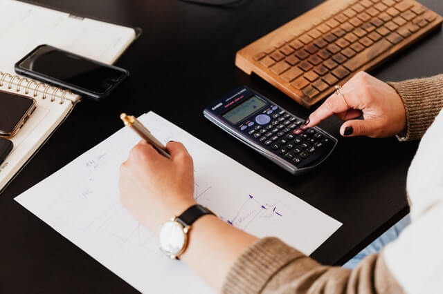 Careers crop woman using calculator and taking notes on paper